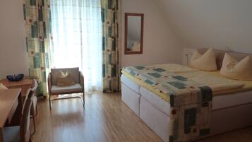 Un dormitorio con cama, una silla, una mesa y un espejo.