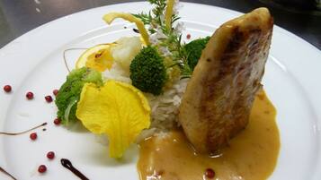 A plate of food with rice, broccoli, cauliflower, and a piece of meat, garnished with sauce and small red berries.