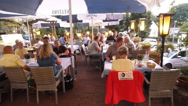 An outdoor dining area with tables and chairs, umbrellas, and street lamps. - Landhaus Sassenhof (Muelheim an der Ruhr)