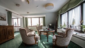 A spacious room with a green patterned carpet, a round wooden table, and four upholstered armchairs. There is a wooden cabinet and a television on a stand. - Landhaus Sassenhof (Muelheim an der Ruhr)