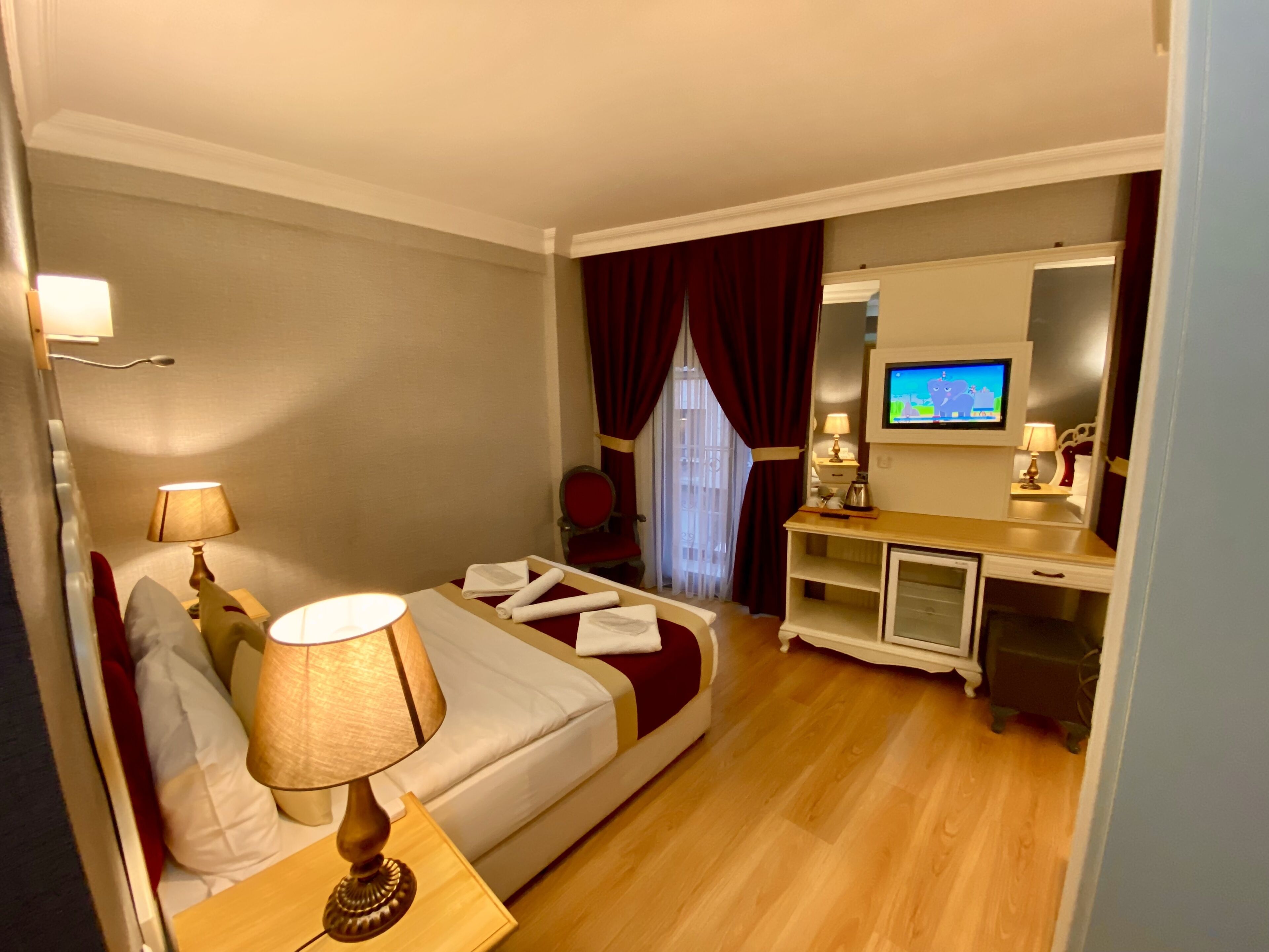 A hotel room with a bed, bedside lamps, a desk with a television, and a mirror.