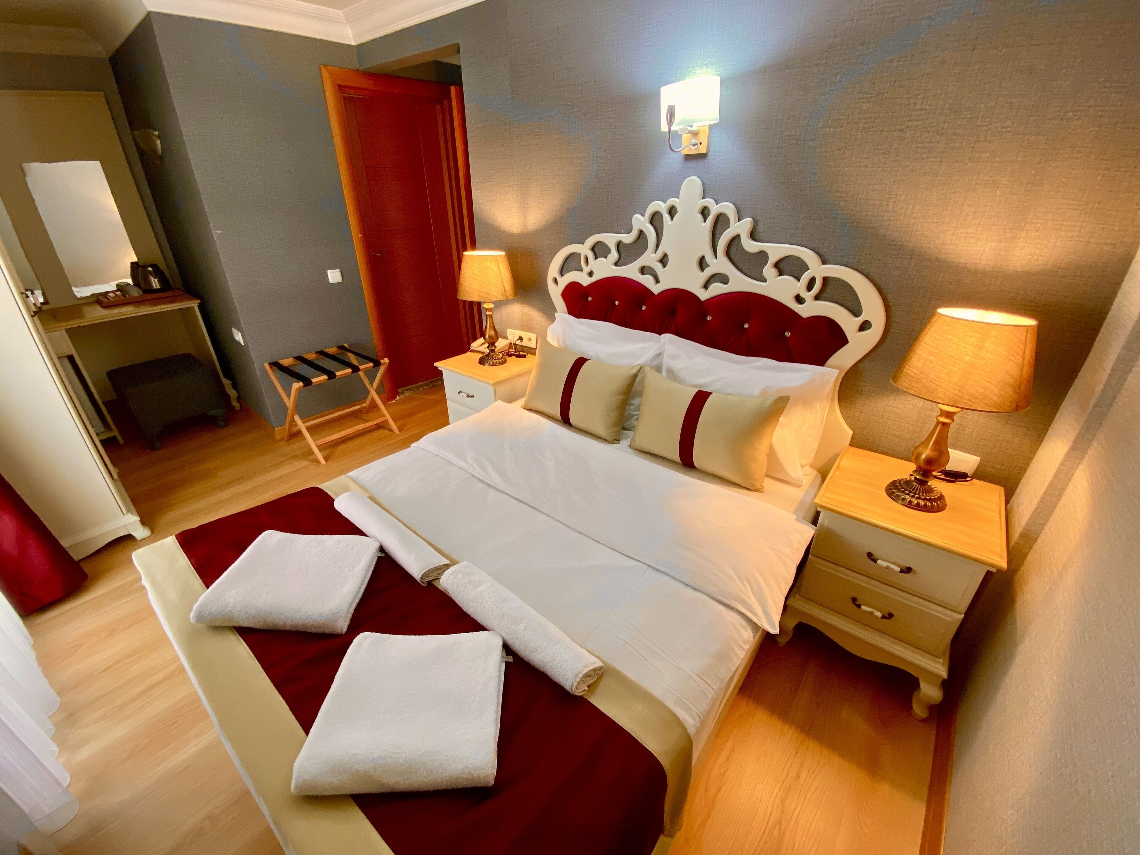 Una camera d'albergo con un letto grande, due comodini, una tenda rossa, una scrivania e una sedia.
