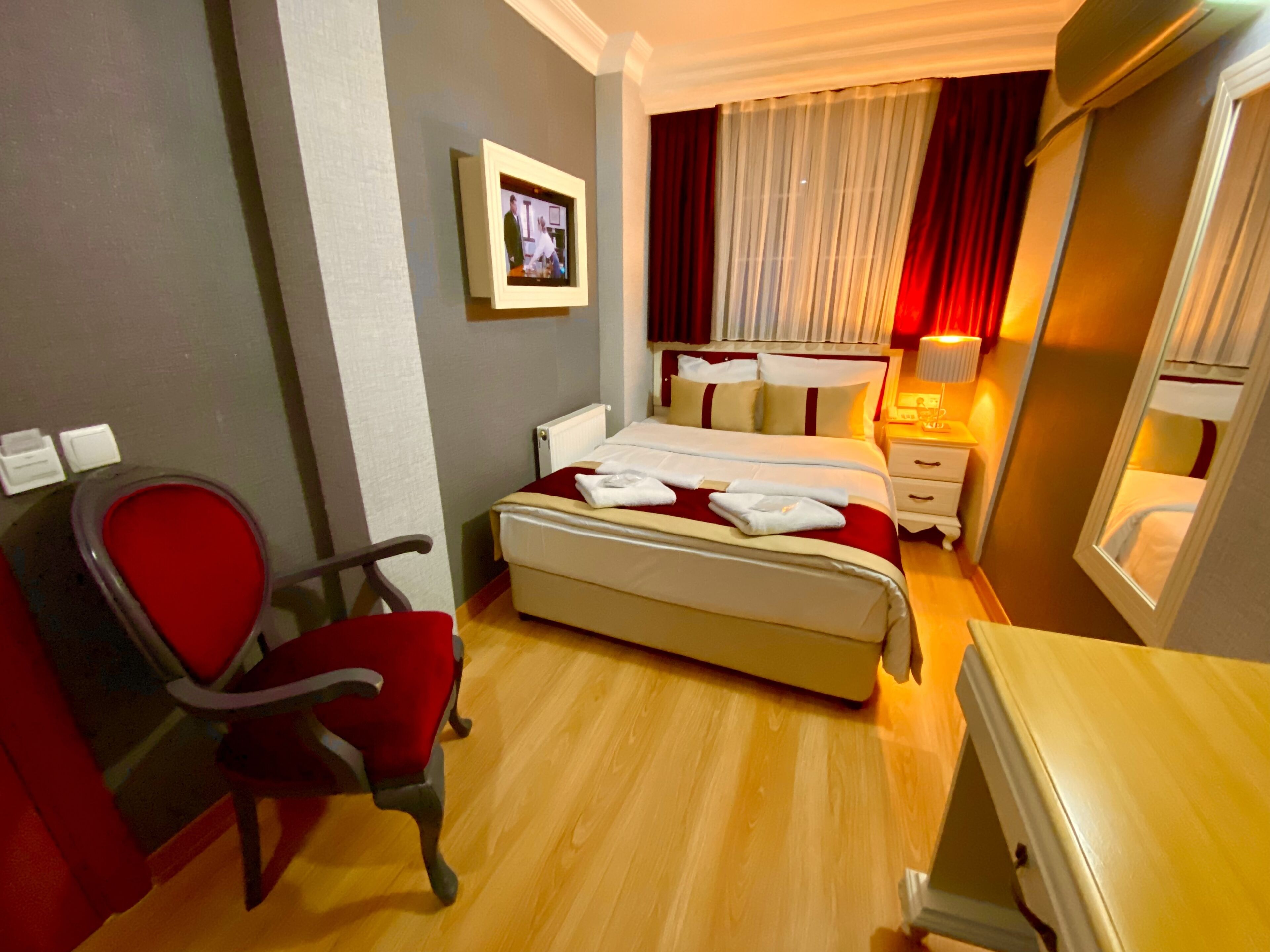 A hotel room with a bed, a chair, a bedside table, a lamp, and a television on the wall.