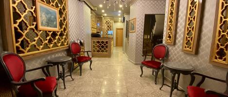 A lobby with marble flooring, red upholstered chairs, and decorative wall panels.