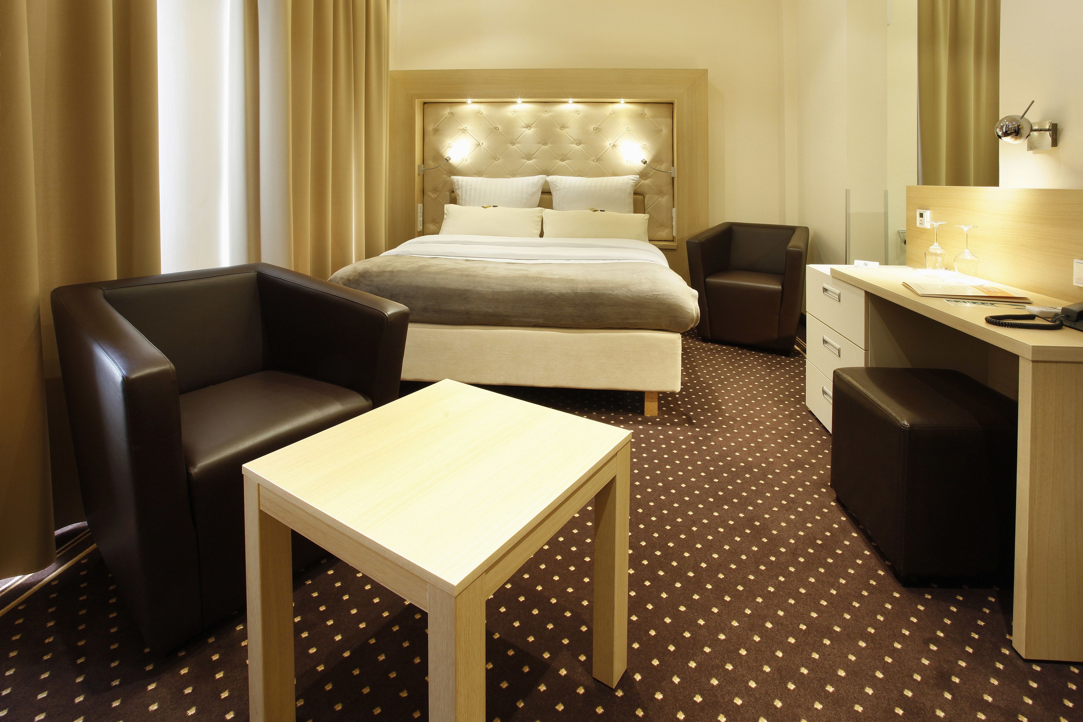 A hotel room with a bed, a desk, a chair, and a small table.