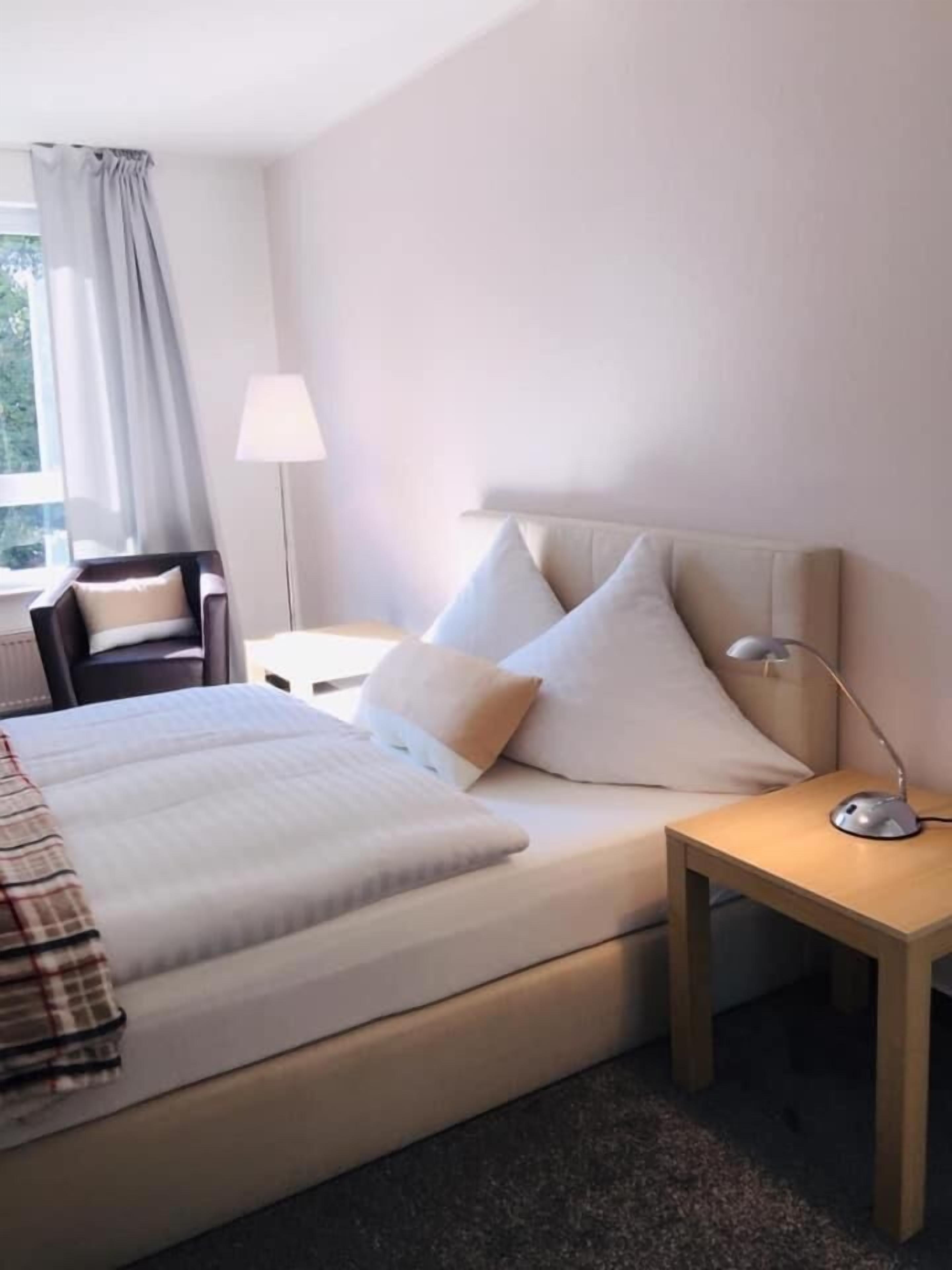A hotel room with a bed, bedside tables, a lamp, and a chair.