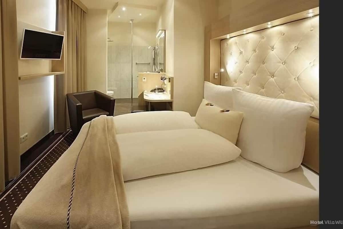 Camera d'albergo con un letto grande, una scrivania, una sedia, una televisione e un bagno con uno specchio e un lavandino.