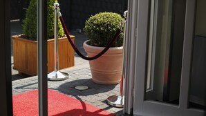 A hotel entrance with a red carpet, a potted plant, and a red rope barrier. - Hotel Villa Will (Isernhagen)