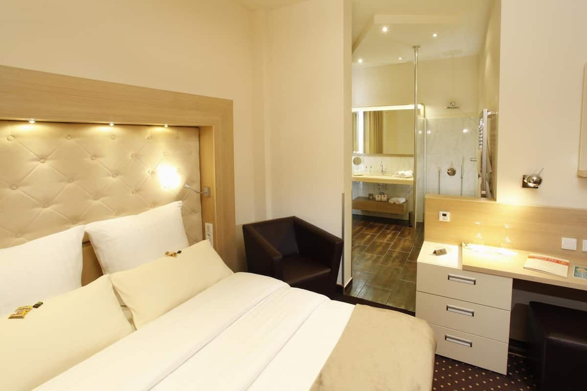 Camera d'albergo con un letto grande, una scrivania, una sedia e bagno visibile tramite una porta in vetro.