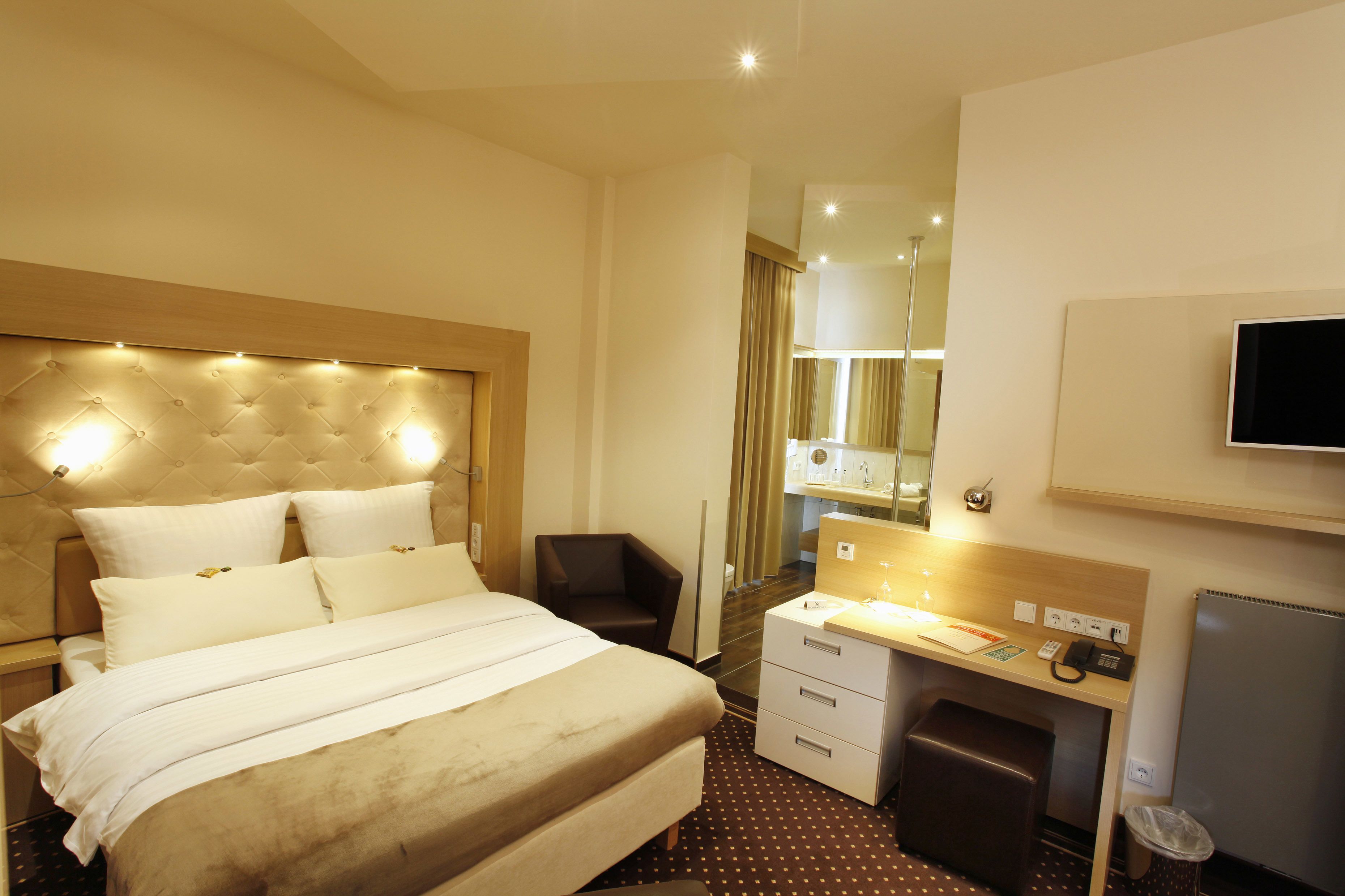 A hotel room with a large bed, a desk with a chair, a television, and a small trash bin.