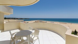 A balcony with a table and chairs, overlooking a beach with a clear sky. - TURIM Algarve Mor Hotel (Portimão)
