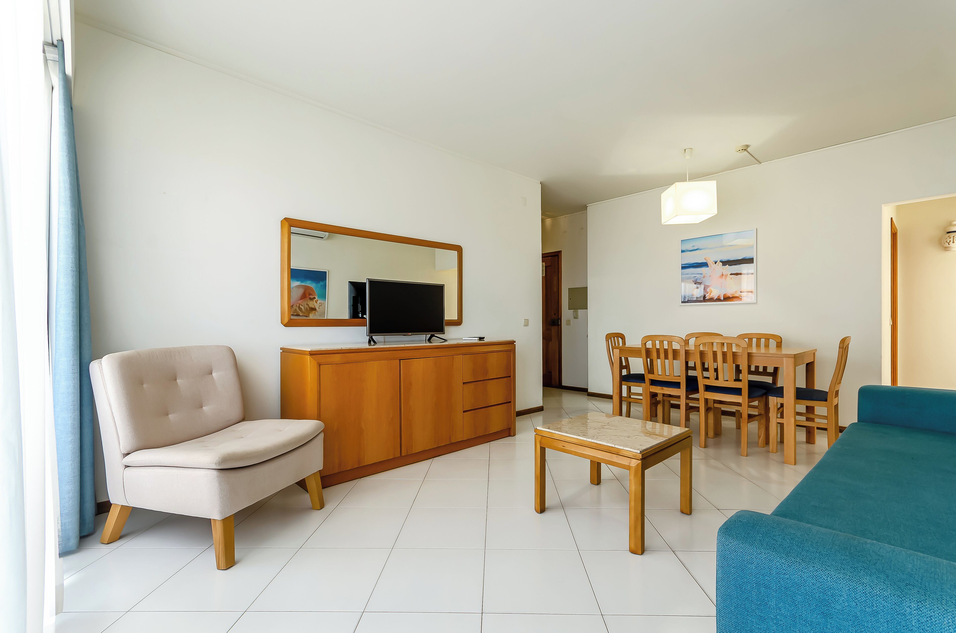 A living room with a sofa, a TV, a dining table with chairs, and a wooden cabinet.