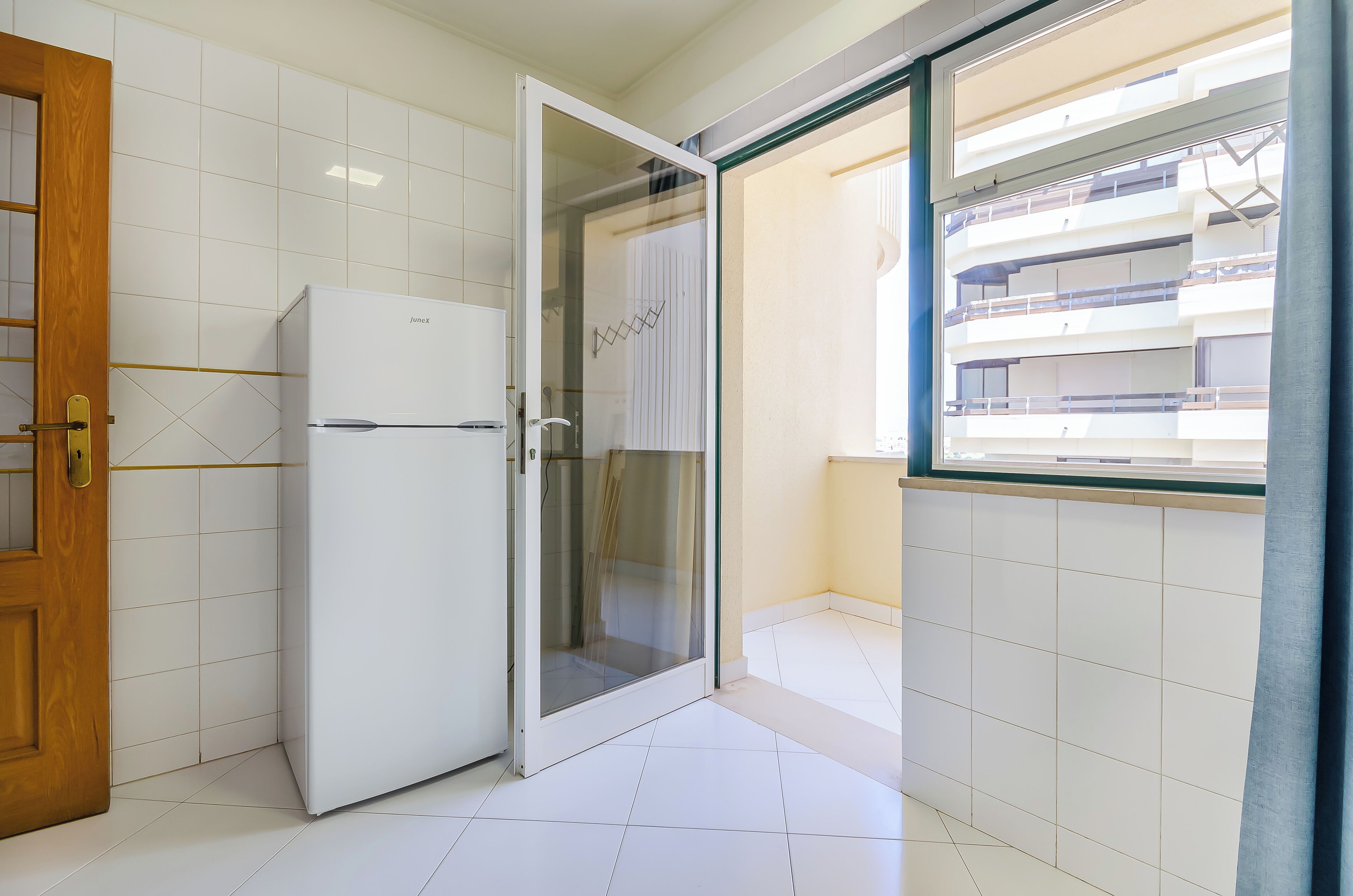 A compact kitchen with a white refrigerator, a glass shower enclosure, and a window with a view of a building.