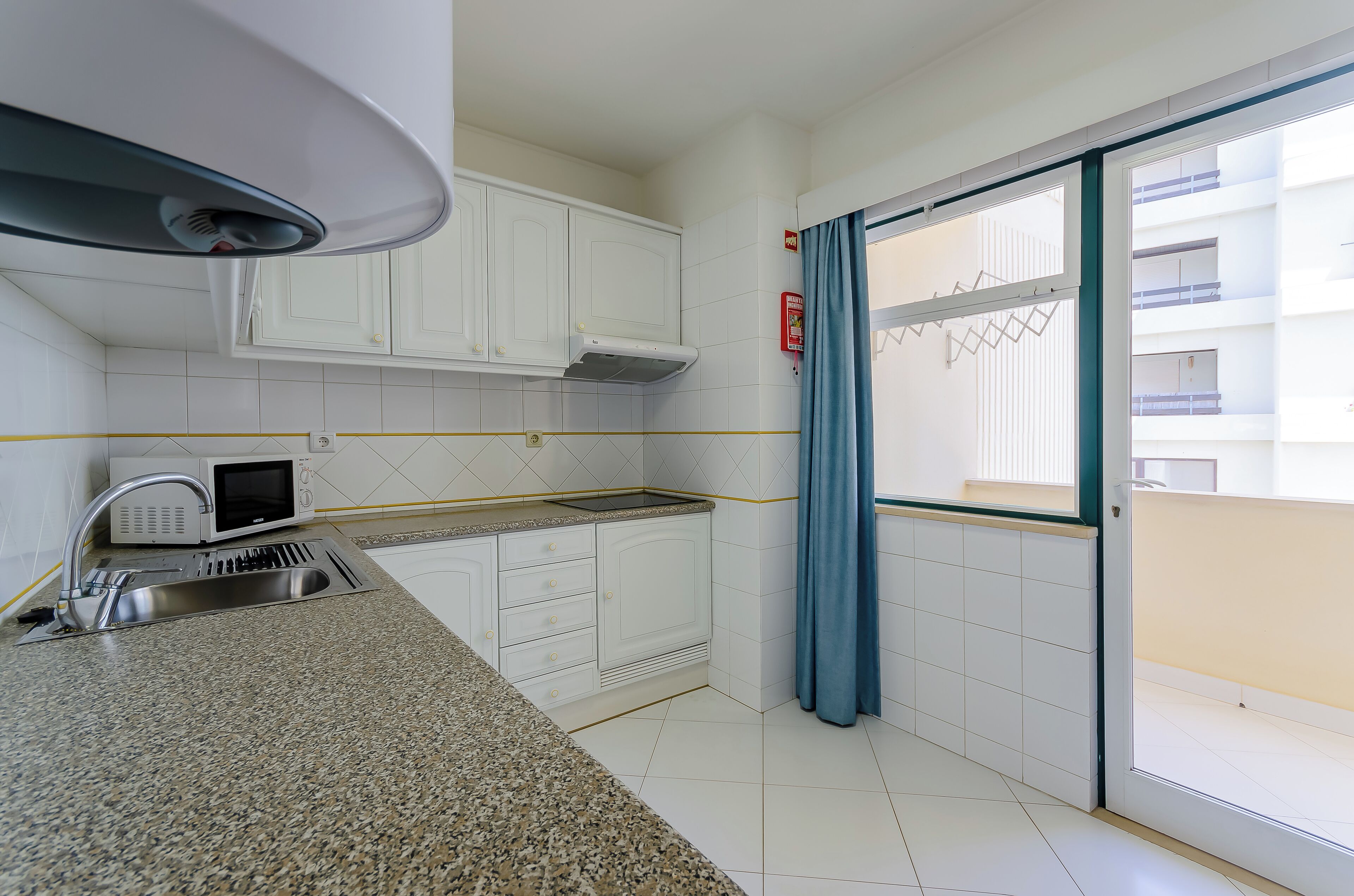 A compact kitchen with white cabinets, a microwave, a sink, and a window with a view of a building.