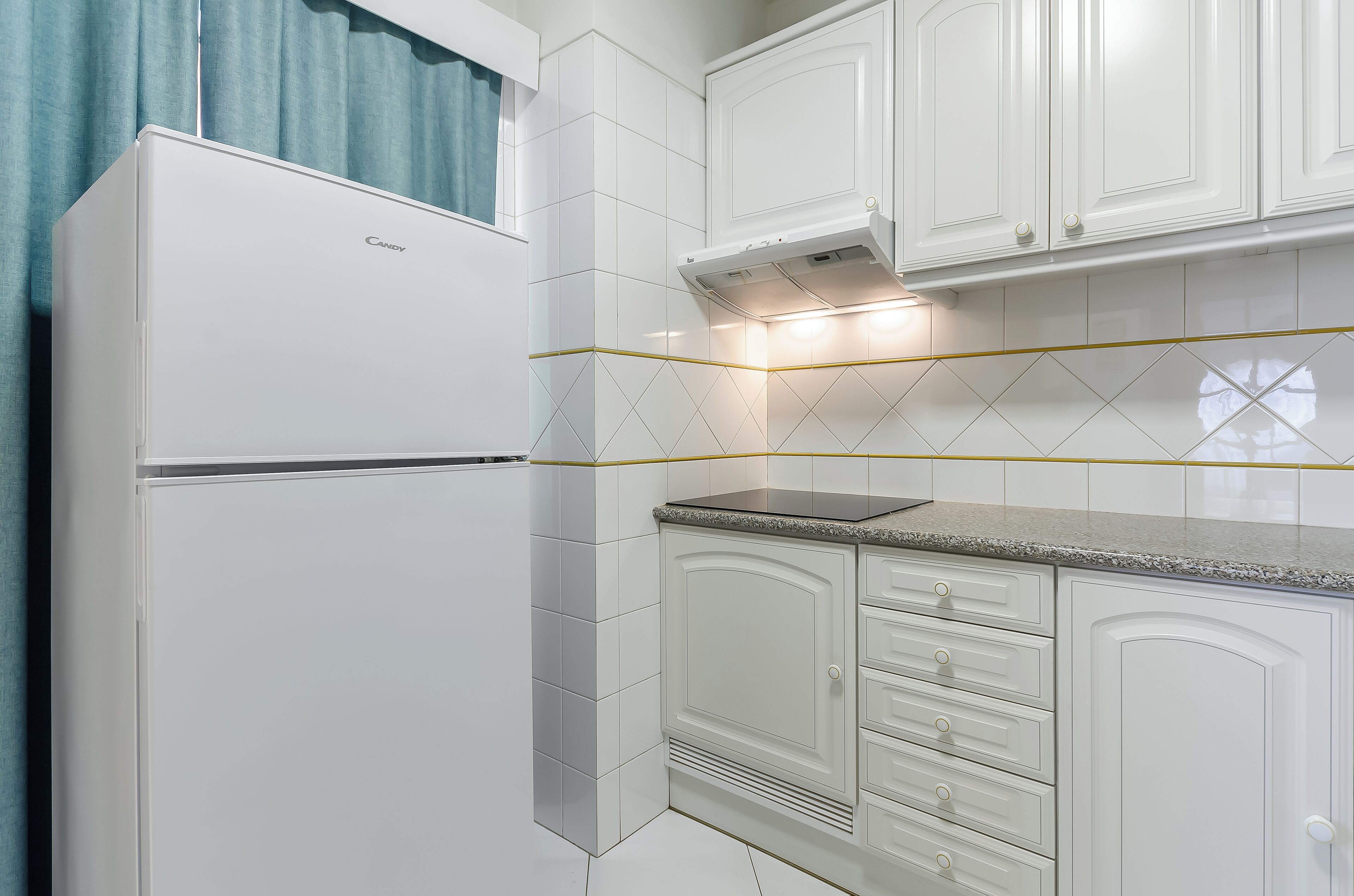 Una cocina con armarios blancos, un refrigerador y una encimera.