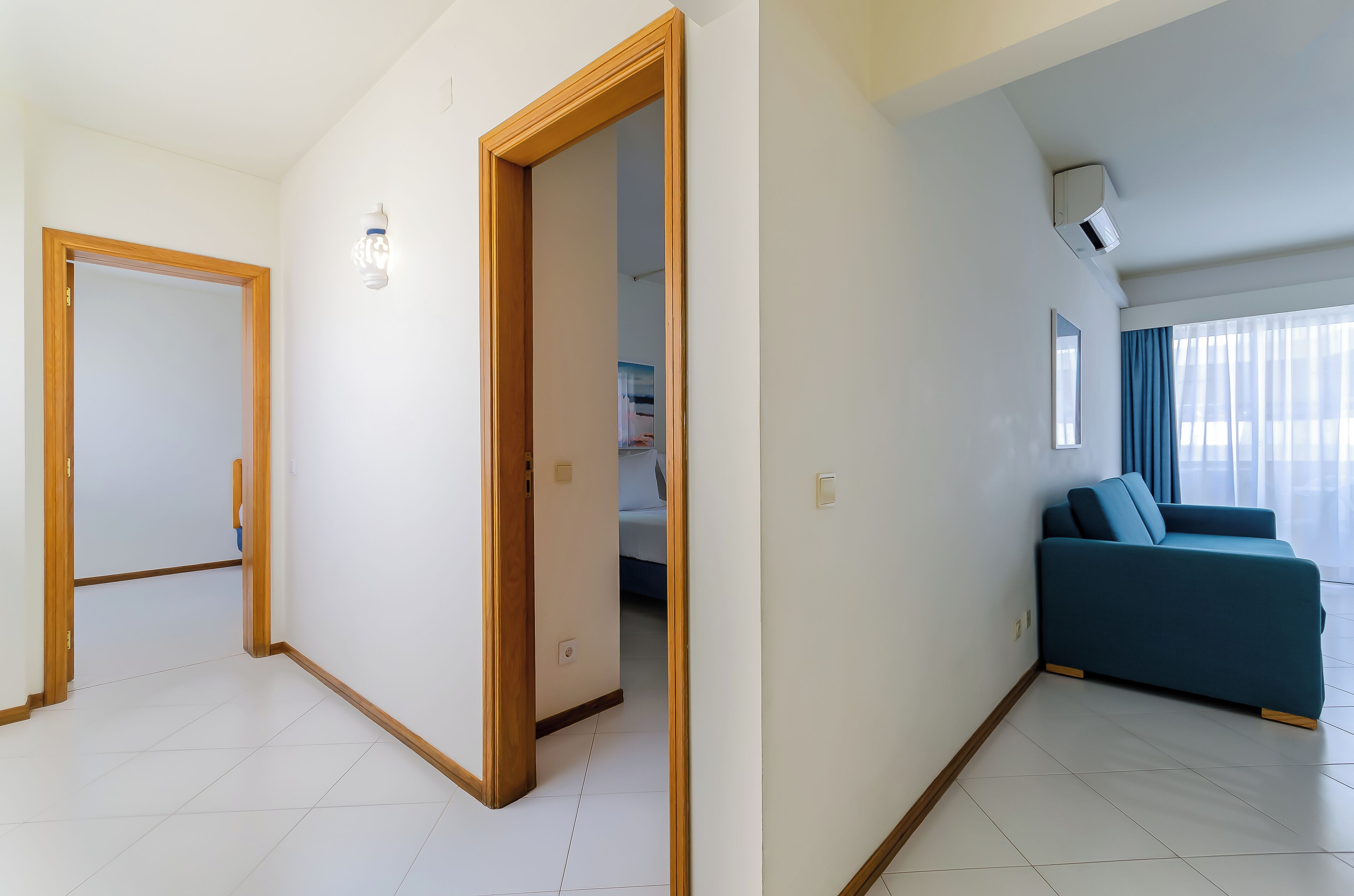 A modern living room with a sofa, a door leading to another room, and an air conditioning unit on the wall.