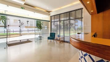 Eine geräumige Lobby mit einer Rezeption, einem grünen Sessel und einem kleinen Tisch mit einem Glas.