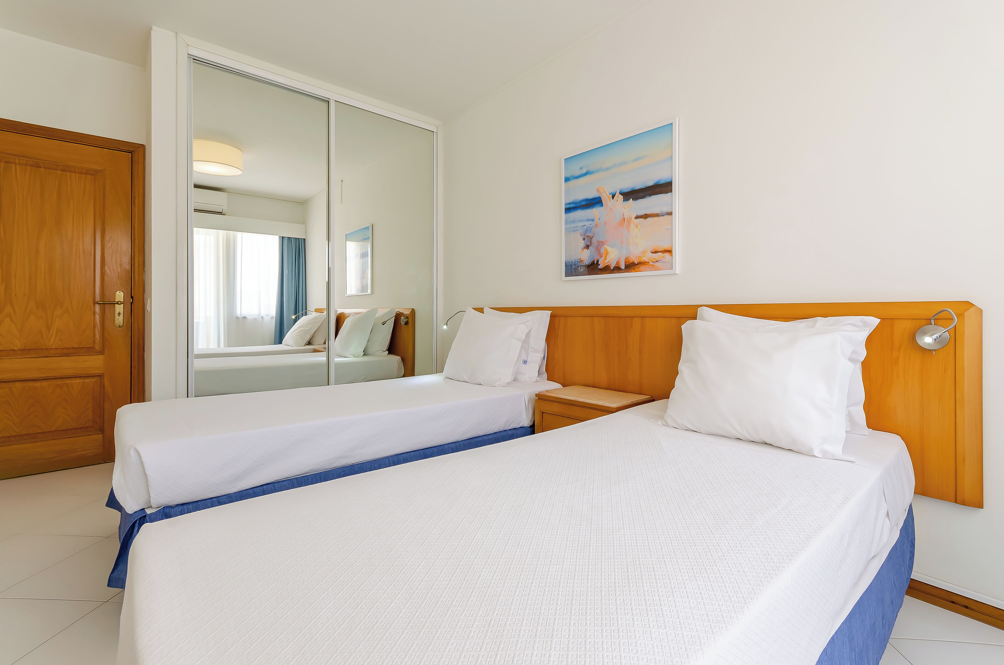 Ein Hotelzimmer mit zwei Betten, einem hölzernen Kopfteil, einem großen Spiegel und einem Bild an der Wand.