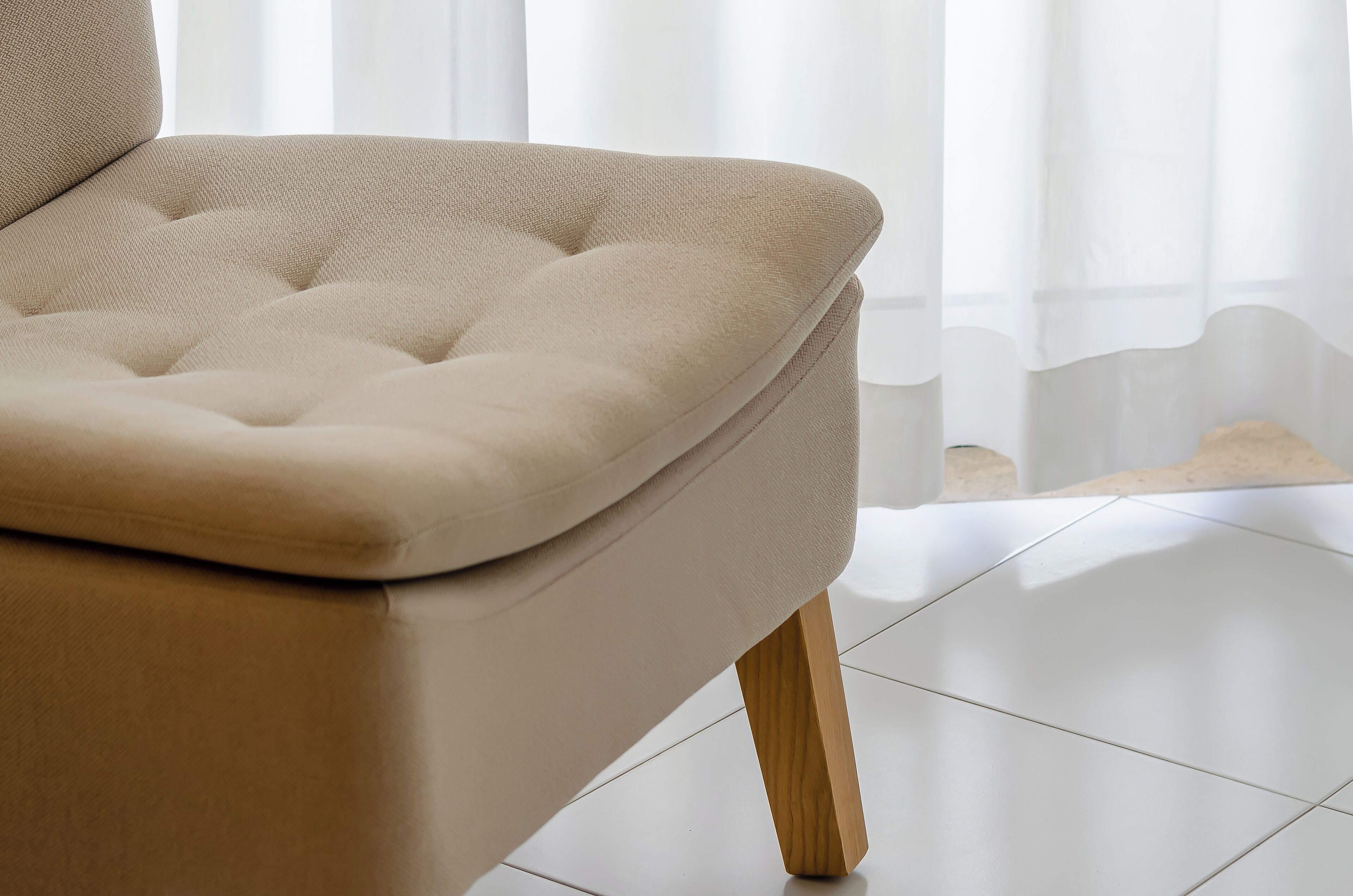 A beige upholstered chair with wooden legs and a cushioned backrest.