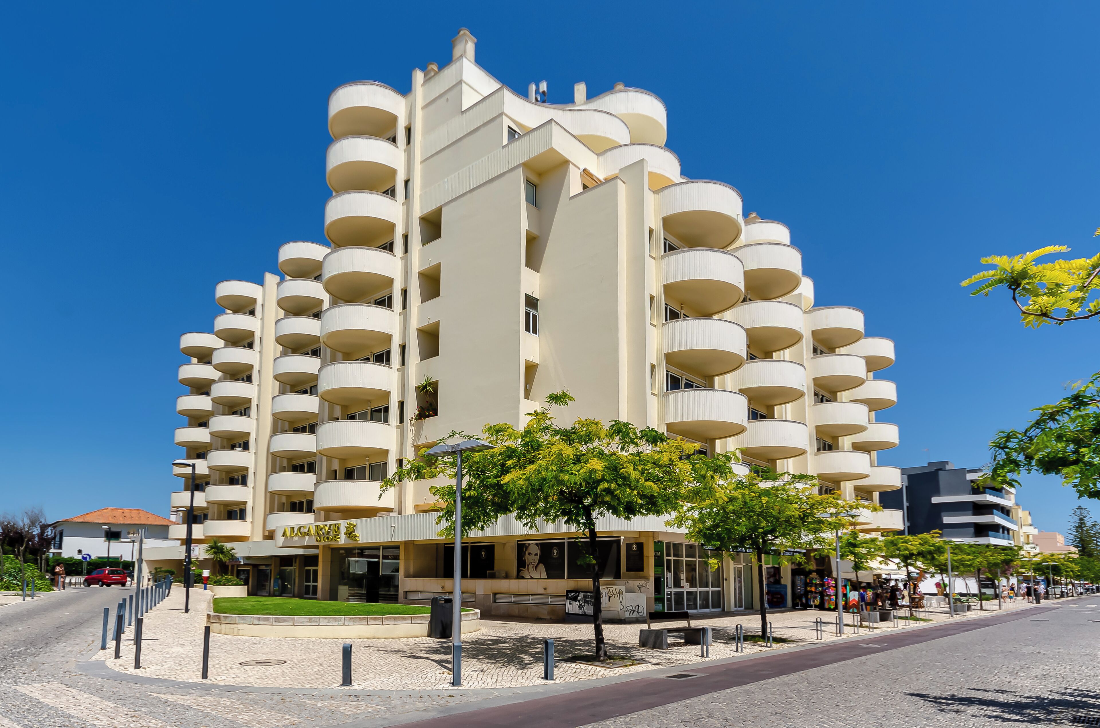 A modern multi-story building with balconies, a cafe, and a street view.