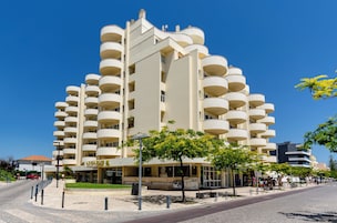 Un edificio moderno de varios pisos con balcones, una cafetería y vista a la calle.