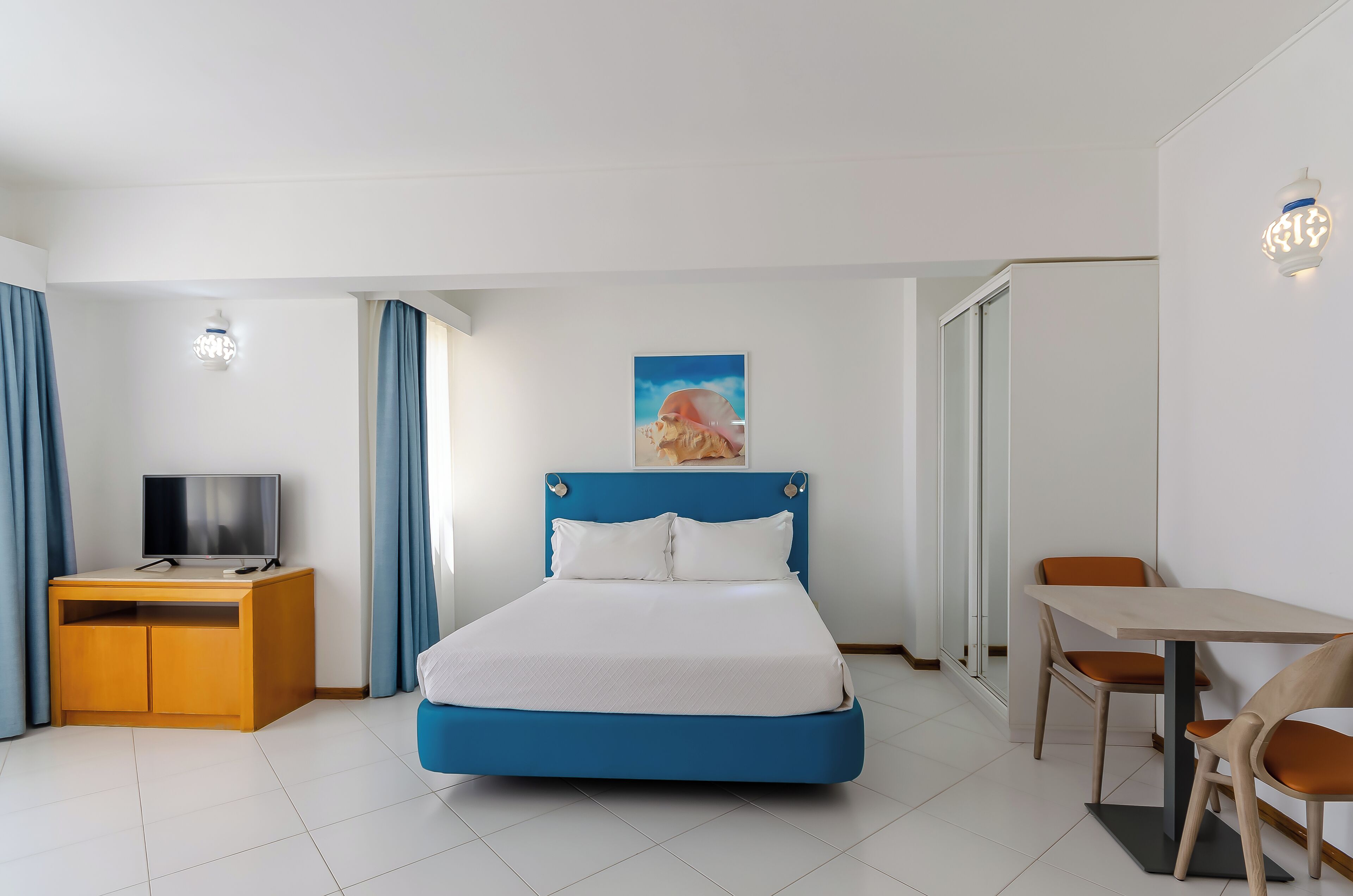 A hotel room with a bed, a desk, a television, and a dining area.