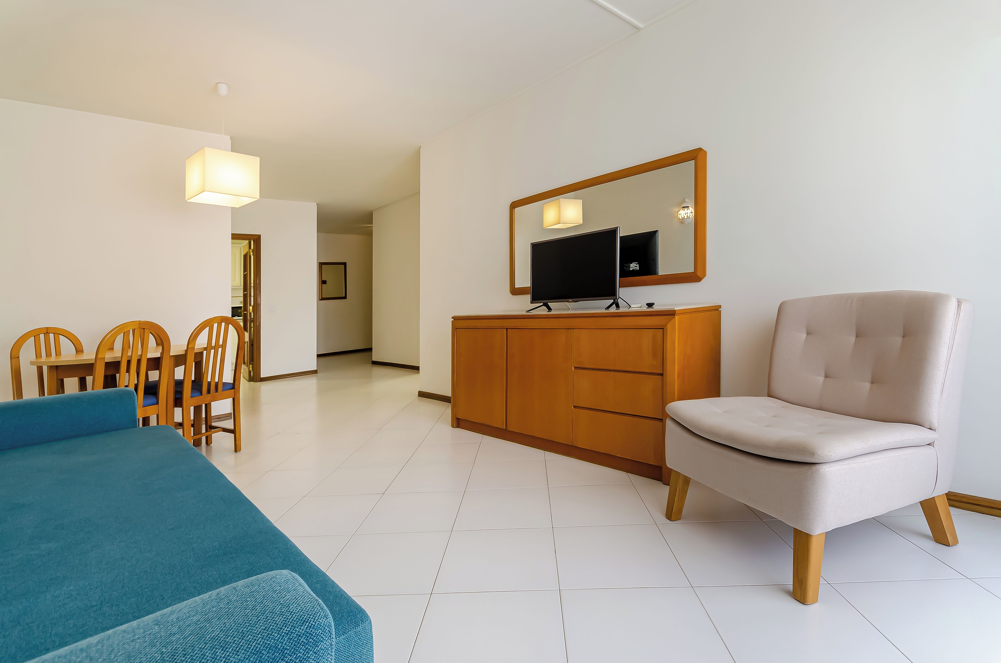 A hotel room with a bed, a chair, a TV, a dresser, and a dining area with chairs and a table.