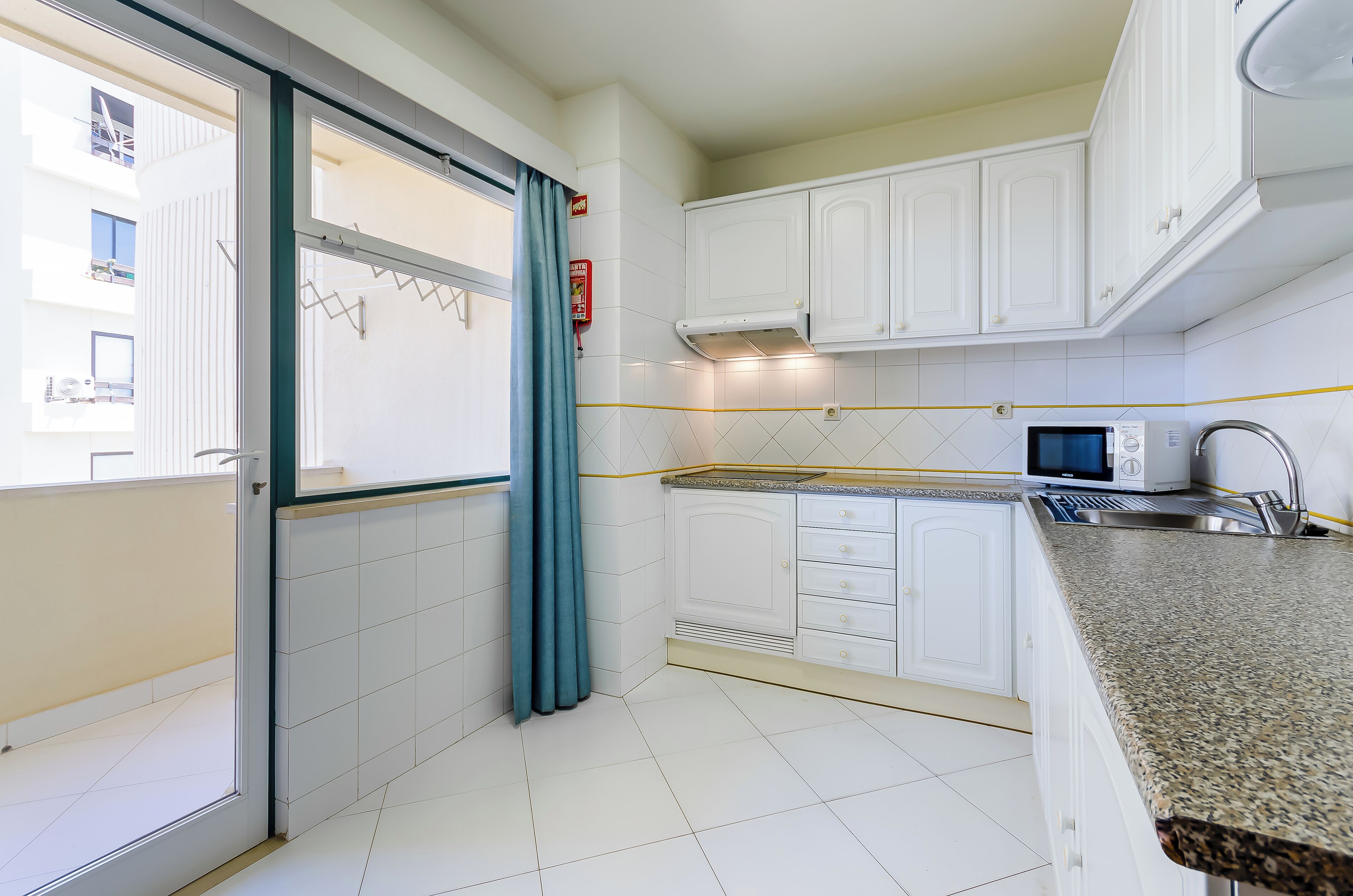 A compact kitchen with white cabinets, a microwave, and a stainless steel sink.
