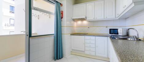 A compact kitchen with white cabinets, a microwave, and a stainless steel sink.
