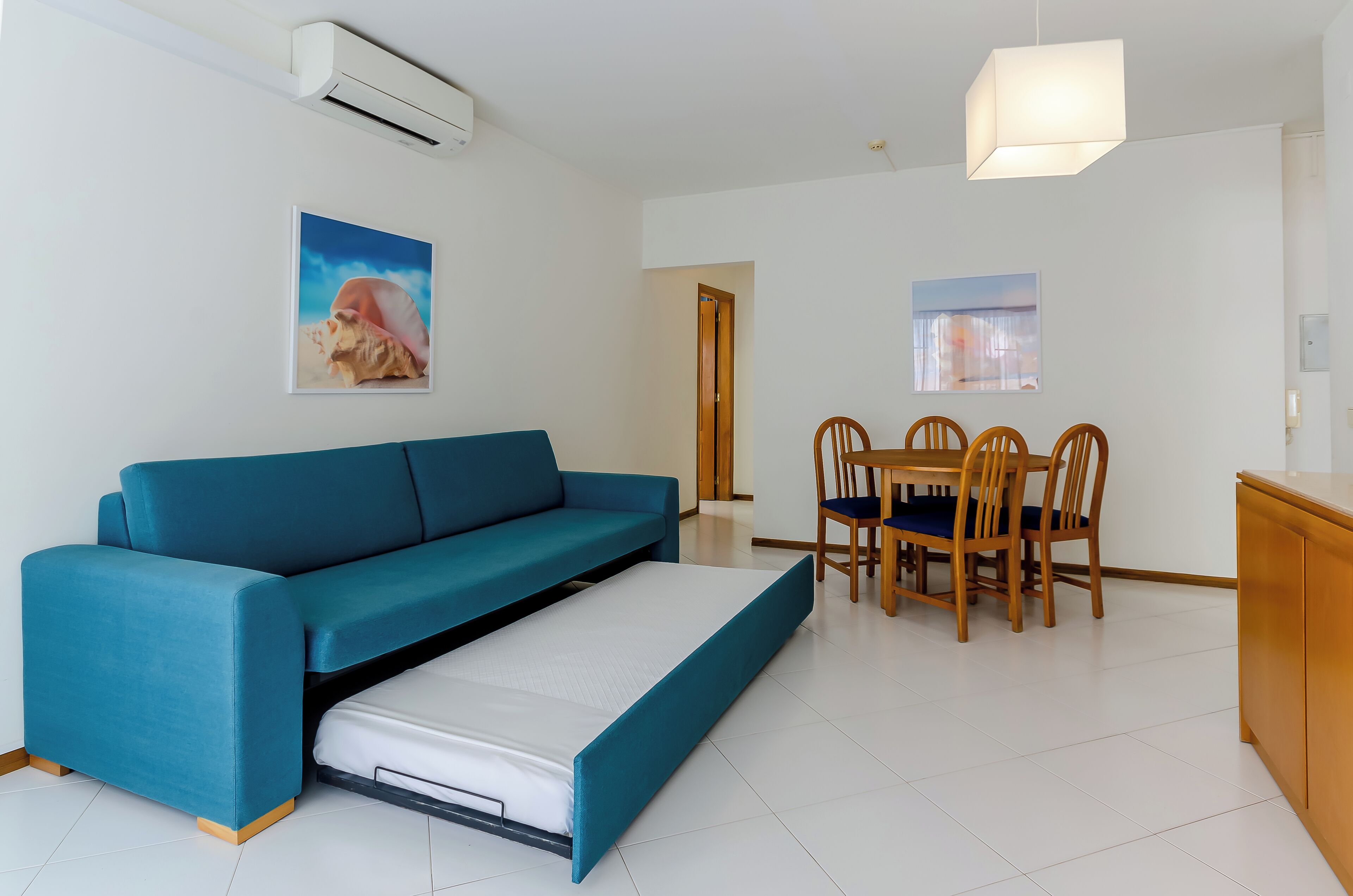 A modern living room with a sofa, a dining table with chairs, and a small kitchen area.