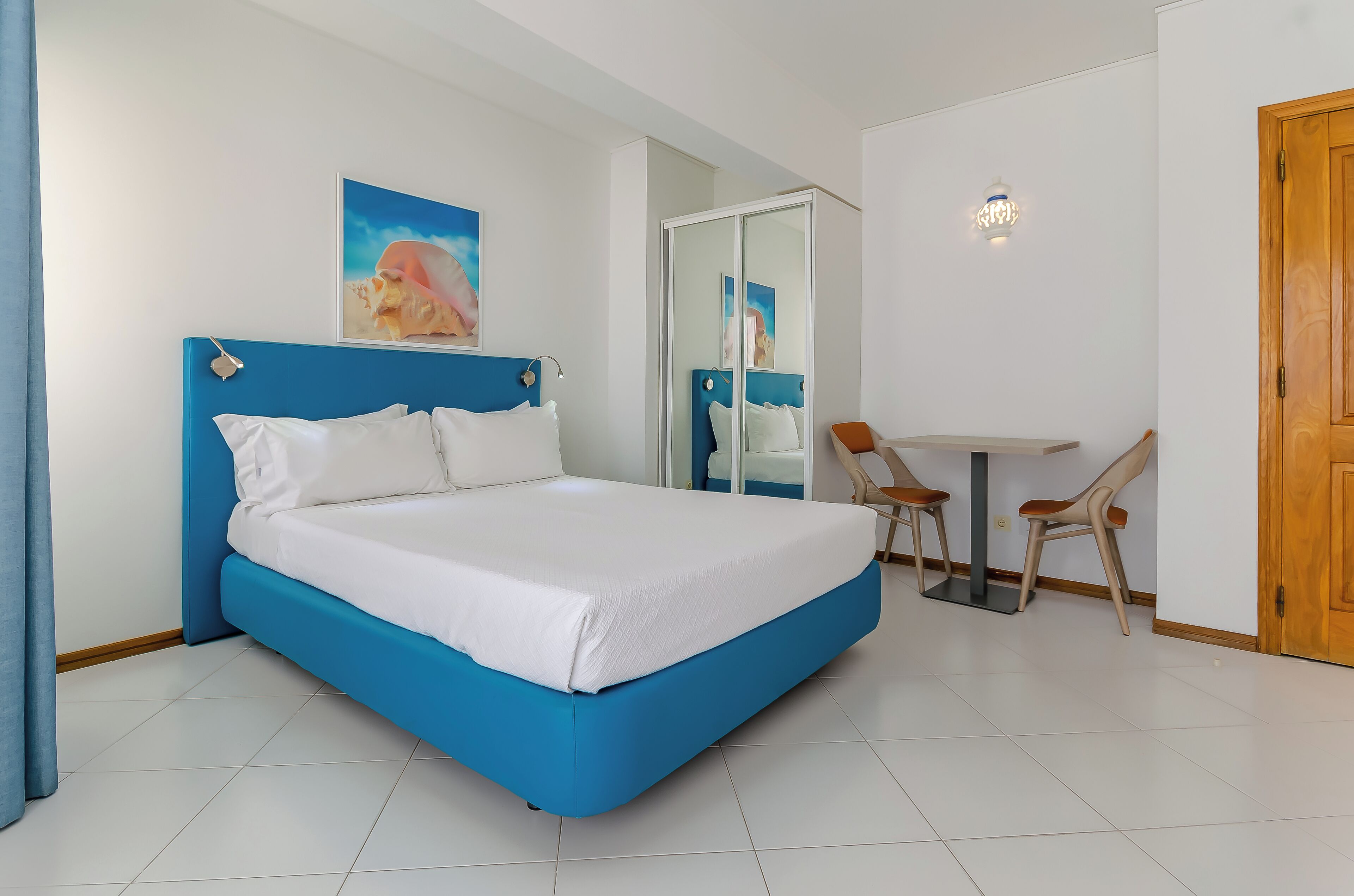 A bedroom with a bed, a desk, chairs, and a door.