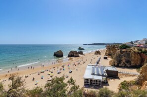 Una playa con formaciones rocosas, una orilla arenosa y un edificio con techo inclinado.