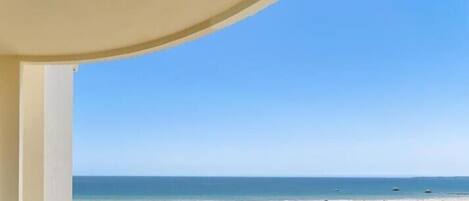 Vista a la playa desde una ventana con arena dorada y cielo azul despejado.