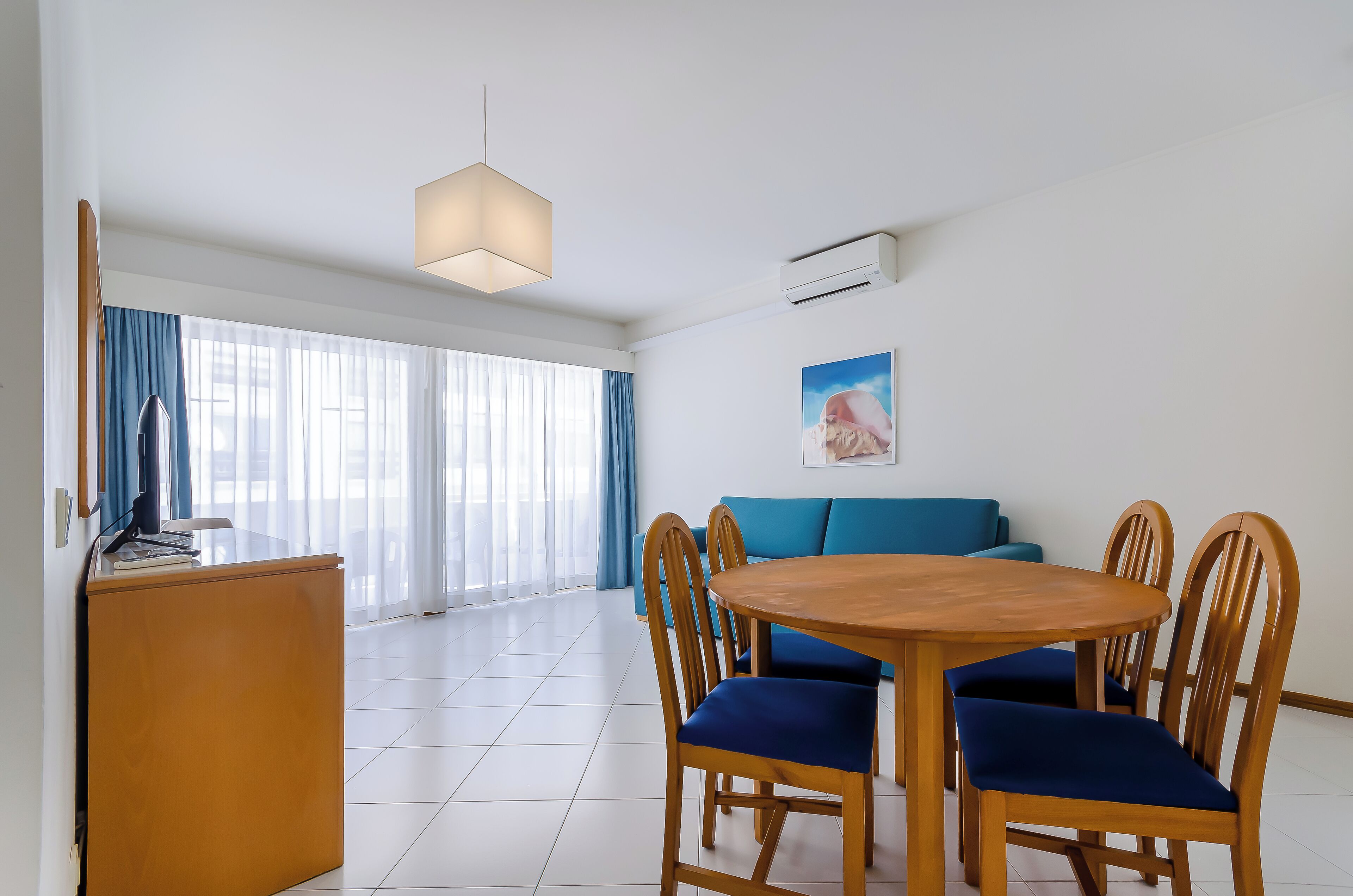 A modern dining area with a wooden table and chairs, a blue sofa, and a large window with curtains.