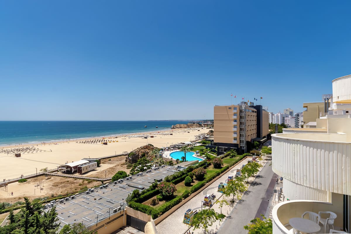 A hotel with a pool, beach view, and a parking area.