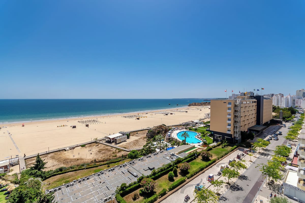 A coastal hotel with a beach view, a swimming pool, and a parking lot.