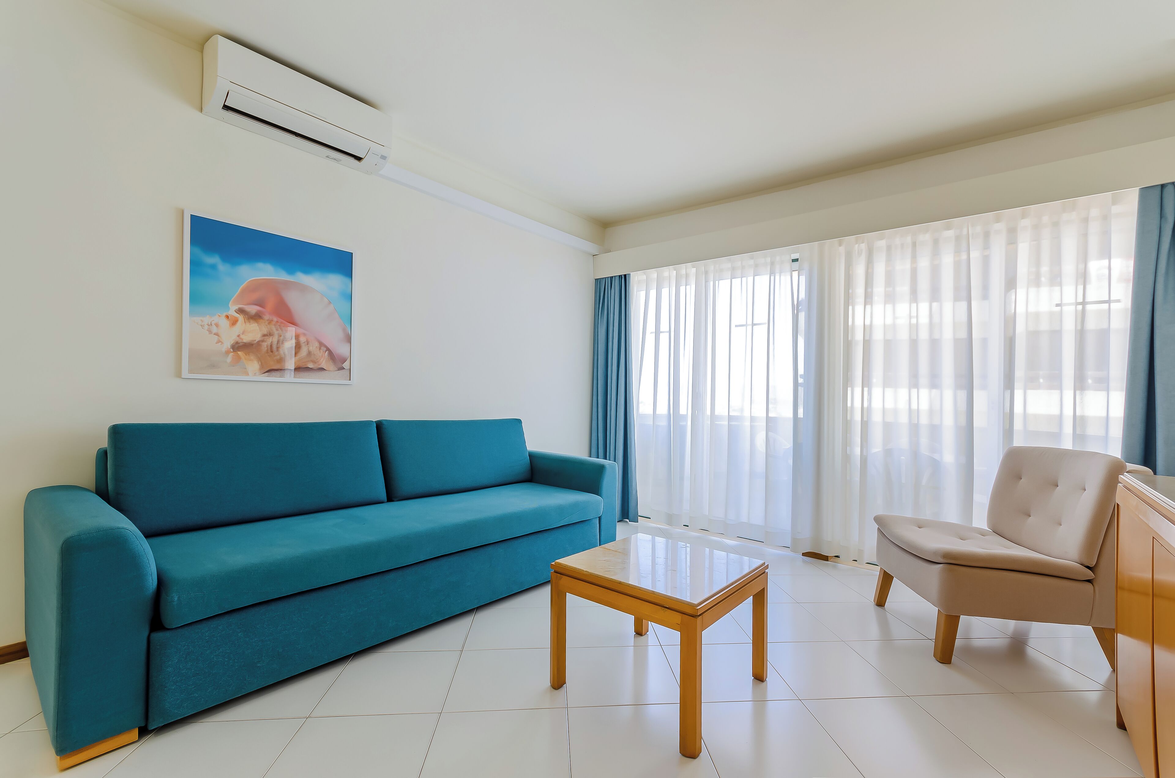 Un salon avec un canapé de couleur turquoise, une table basse en bois, un fauteuil beige et un tableau accroché au mur.