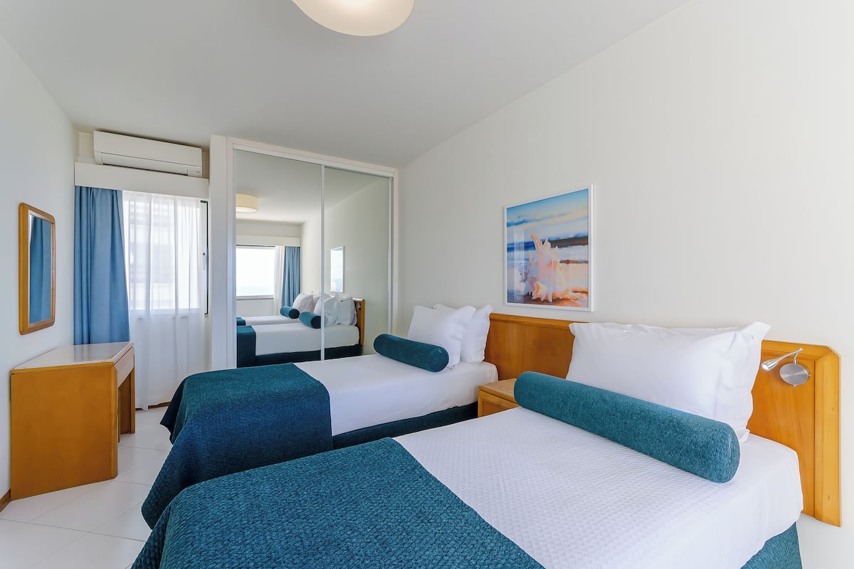 A hotel room with two beds, a desk, a chair, a mirror, and a painting on the wall.