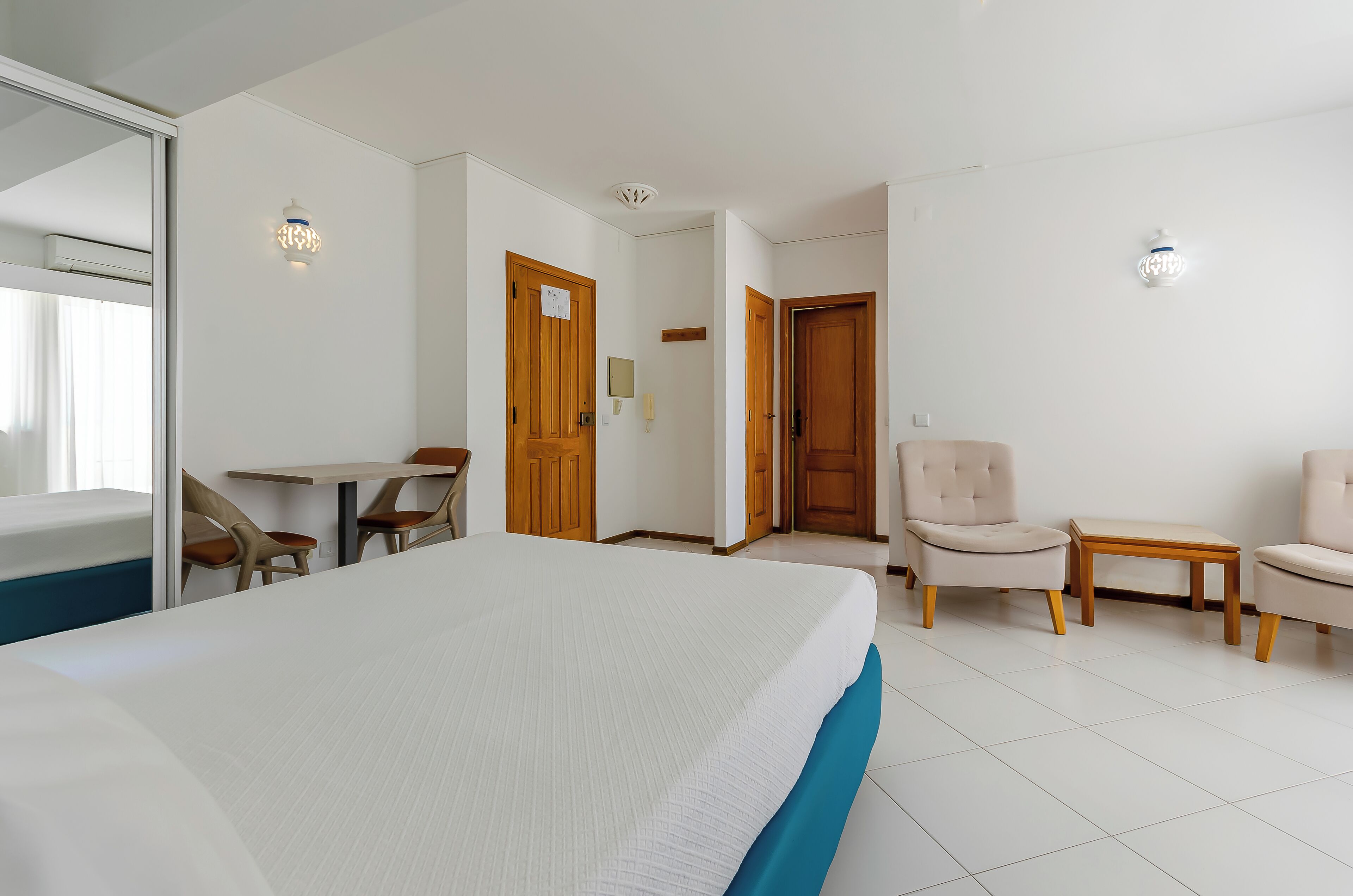 A hotel room with a bed, two chairs, a small table, and a door.