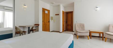 A hotel room with a bed, two chairs, a small table, and a door.