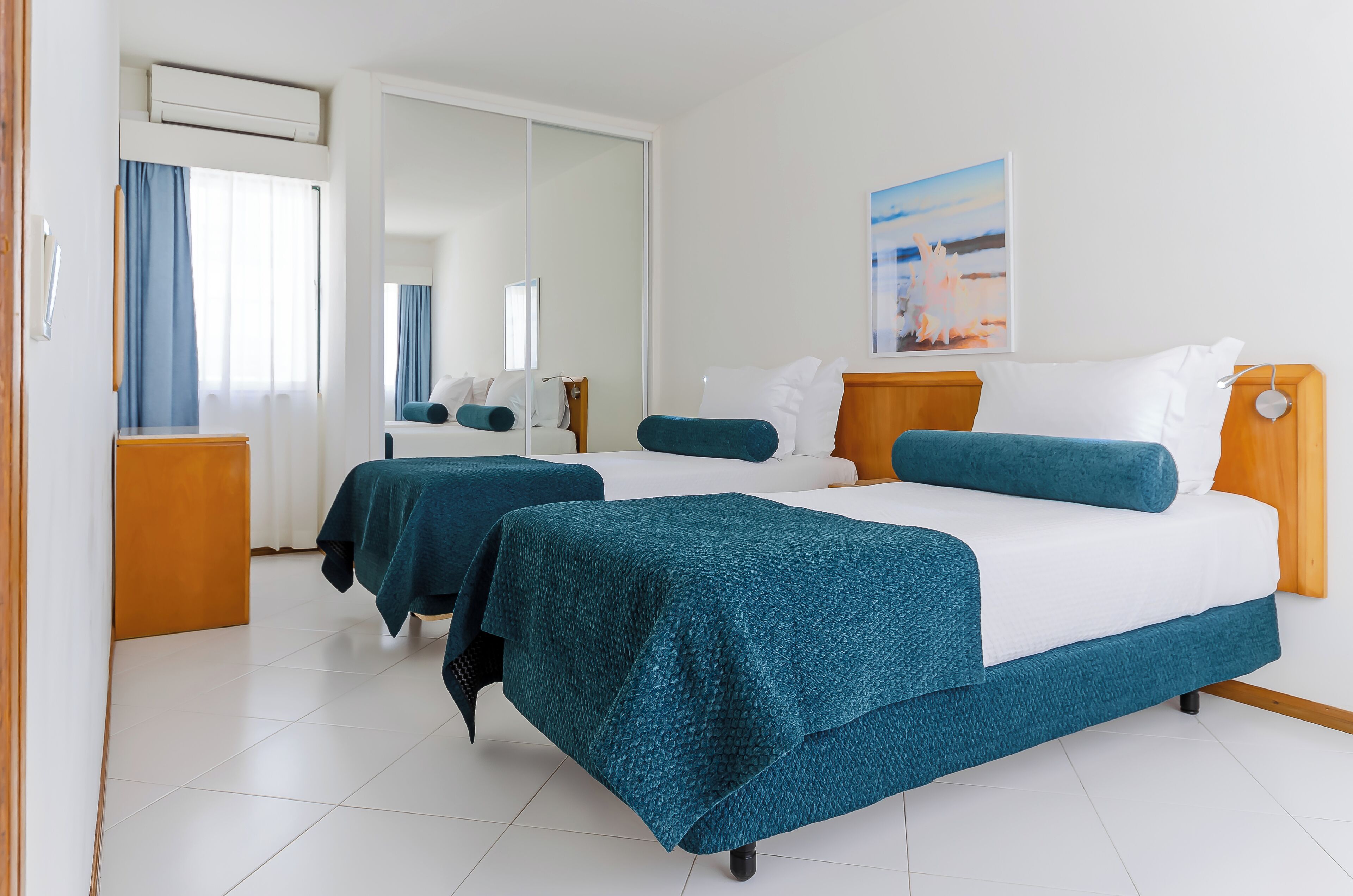 A hotel room with two beds, a wooden headboard, a large mirror, and a painting on the wall.