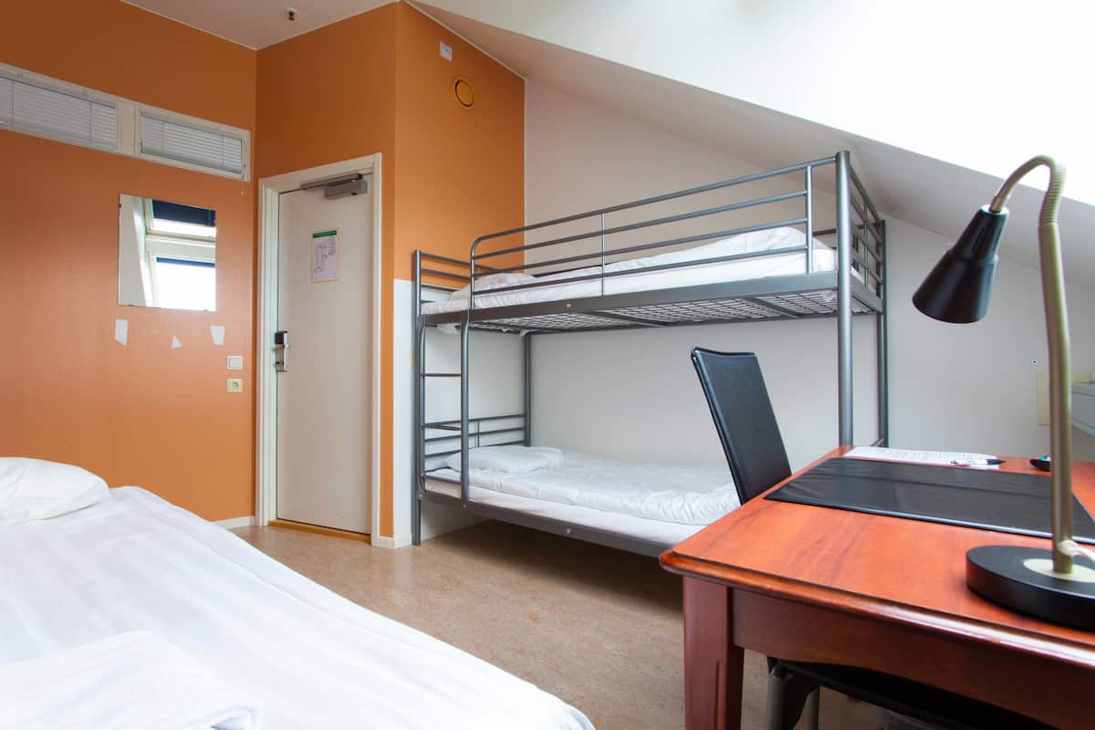 A room with a bunk bed, a desk with a lamp, and a bed with white bedding.