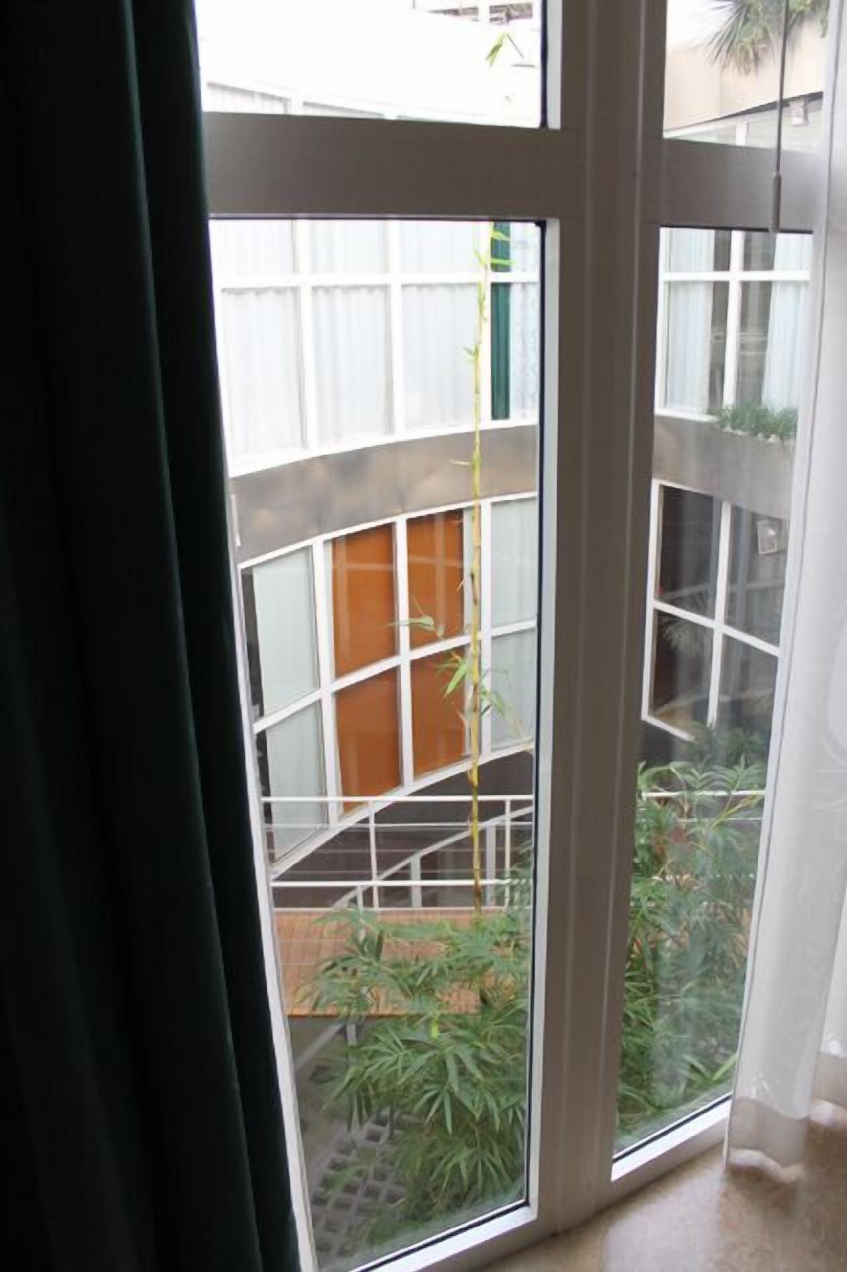 Vista a través de una ventana con una planta de bambú, un banco de madera y una baranda de metal.