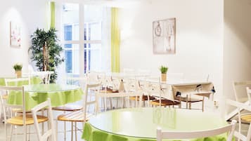A conference room with round tables, white chairs, and green tablecloths. There are potted plants and a large window with curtains.