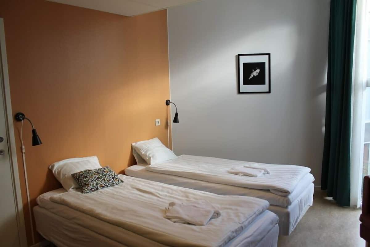 A hotel room with two single beds, a framed picture on the wall, and a window with curtains.