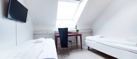 A small, well-lit room with two beds, a desk, and a chair.