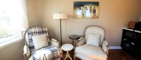 A living room with two armchairs, a floor lamp, a small table, and a painting on the wall.