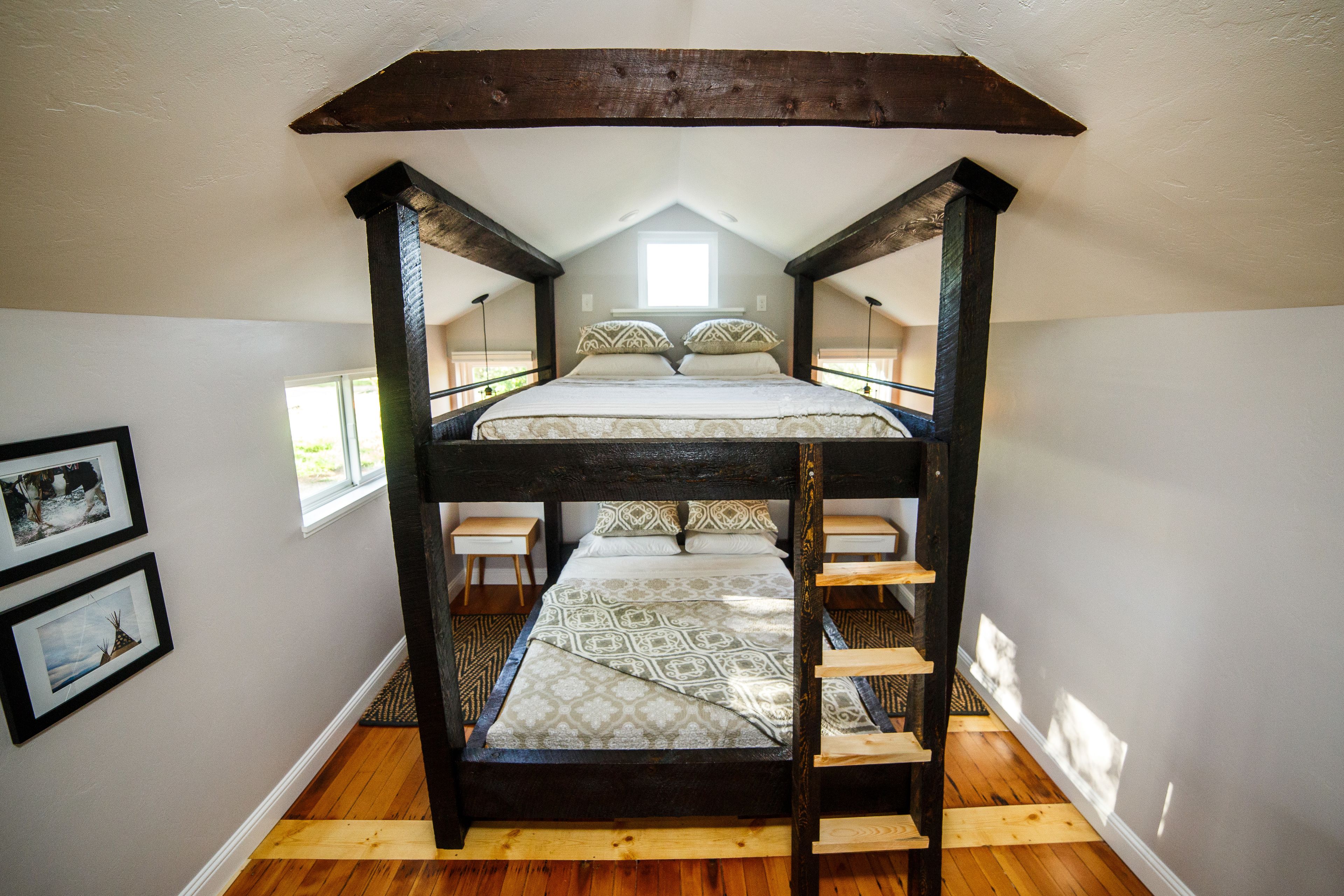 A bunk bed room with a sloped ceiling, wooden beams, and a window providing natural light.