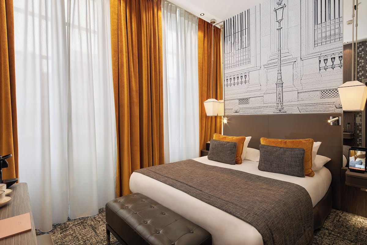 A hotel room with a large bed, a bench, a desk, and a wall-mounted TV.