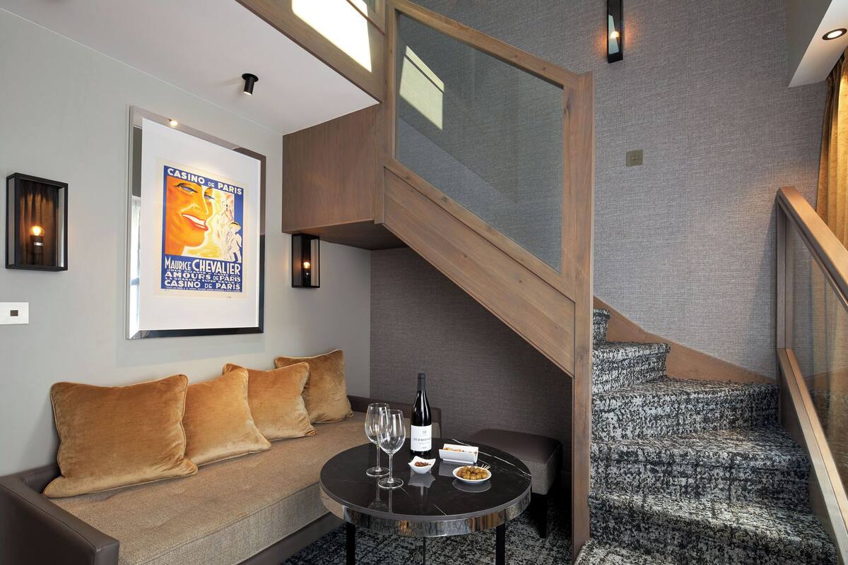 A modern interior with a sofa, a round table with a bottle of wine and glasses, and a staircase with patterned steps.